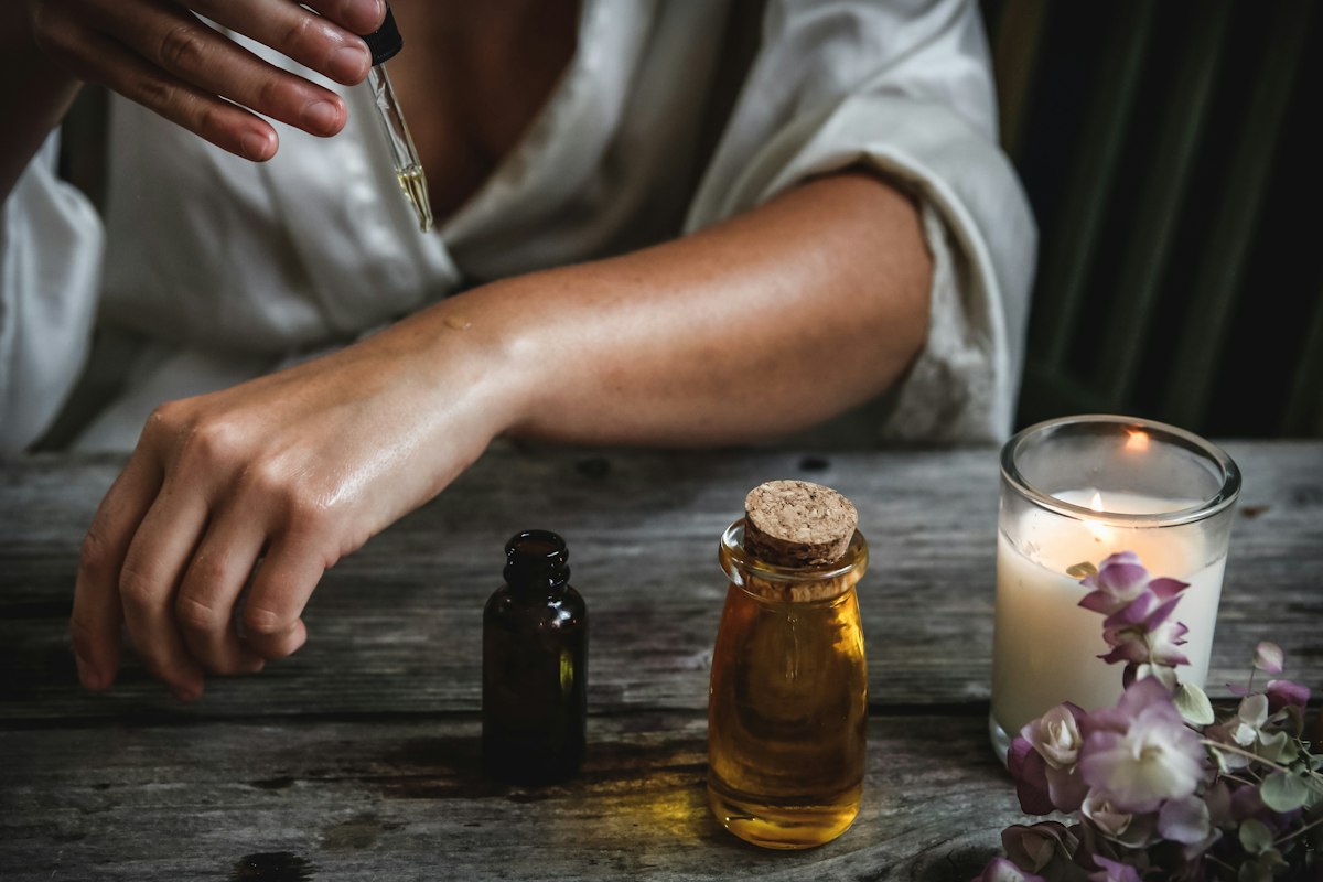 Mains appliquant une huile naturelle, flacons en verre ambré sur une table en bois